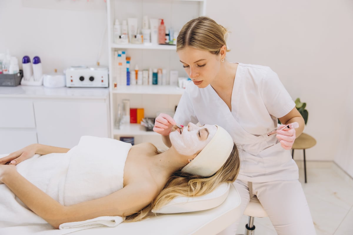 Esthetician carefully applying a facial mask in a serene spa setting